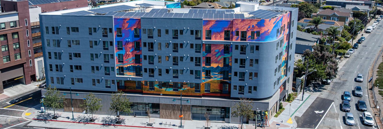 Aerial photo of Nellie Hannon Gateway in Emeryville. Photo shows a 9-story gray building with blue and pink mural.