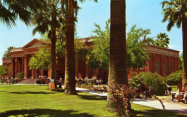 Historic photo of the Carnegie Free Library, Tucson AZ a stately red building with columns and roman design motif behind tall palms and a large grass area