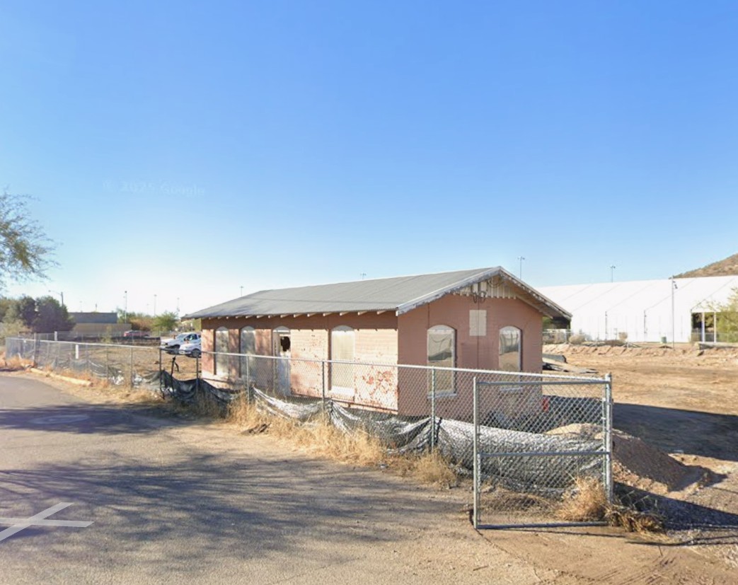 Abandoned brick structure and dirt lot surrounded by chainlink fence at the former Flint Oil site