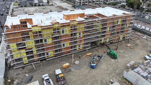 Aerial view of a multi-story building under construction with scaffolding, construction materials, workers, vehicles, and equipment surrounding the site in this shovel ready Brownfield project.
