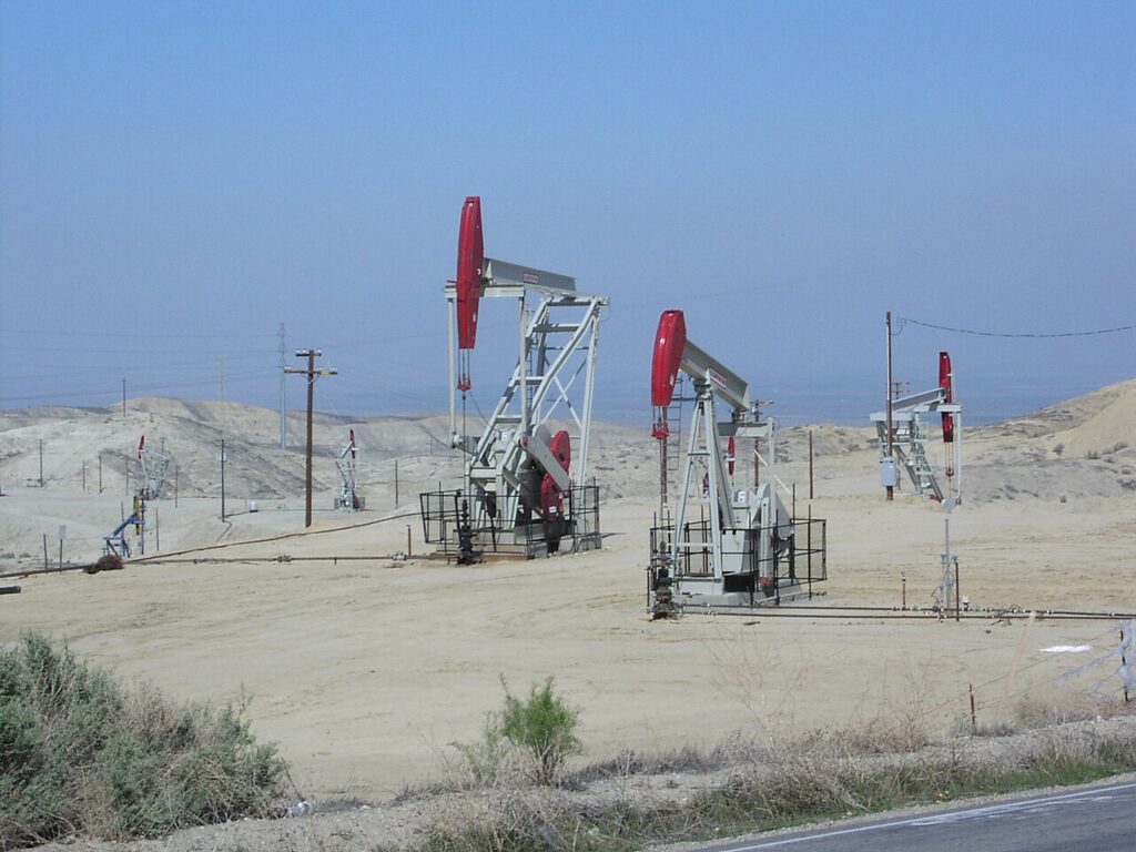 Oil pumpjacks with red tops operate in a dry, sandy landscape of reclaimed land under a clear blue sky, in Elk Hills Oil Field outside of Bakersfield CA