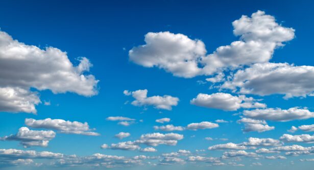 A bright blue sky filled with scattered, fluffy white clouds of various sizes stretches above reclaimed land, creating a peaceful and open atmosphere.